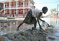 洪水の影響を受けたゴナイブ市の旧市街で、バケツを使って泥と泥水を家から道路にかき出す女の子。