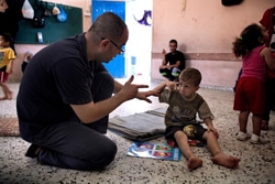 ガザ市のUNRWAが運営する学校に設置された避難所に身を寄せる聴覚障がいのある5歳の子ども。ユニセフのパートナー団体のスタッフと手話で会話をする。