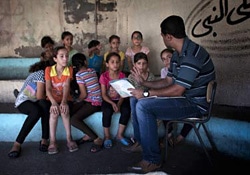 ガザ地区の避難所となっている学校で、避難している子どもたちに読み聞かせを行うボランティア。