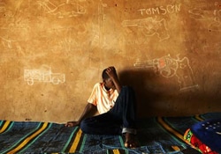 チャド・ンジャメナにあるトランジット・センターで、武器や軍用車両の絵が描かれた壁にもたれて座る少年。