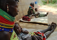 ケニア、ロキチョギオにある保健施設で中度の栄養不良治療を受けた後、診療所の外で、母親のひざの上に座っているナルトム・エセコンちゃん。