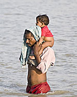 洪水で家が押し流され、子どもを抱えて増水した水の中を歩く男性