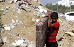 7月21日に、カーンユニス（Khan Yunis）の空爆で破壊されたアブ・ジャマ一家の3階建て家の瓦礫の中から、マットレスを運び出すパレスチナの少年。（ガザ地区）
