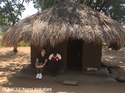 ウガンダ北部への出張で訪れた村の方と一緒に。日干しレンガでできた壁に藁葺き屋根の家が、典型的なウガンダの農村地域の暮らしです。