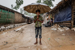 モンスーン期の雨で水が溢れる道に、裸足で立つ難民の男の子。(2018年7月撮影)