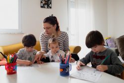 北マケドニアの自宅で1歳のステラちゃんの面倒を見ながら、5歳のマクシムくんとジャンくんの双子の兄弟の勉強を見る母親。(2020年3月25日撮影)