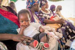 アダマワ州・ヨラの診療所で、母親の膝の上で予防接種を待つ生後4カ月のウィズダムちゃん。(ナイジェリア、2020年1月撮影)