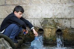 家族のために、村の井戸から汲み上げられた飲用水を容器に入れる11歳のアドハムくん。(2021年3月撮影)