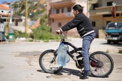 6リットルの容器2つに水を汲み、自転車で家に向かう11歳のアドハムくん。(2021年3月撮影)