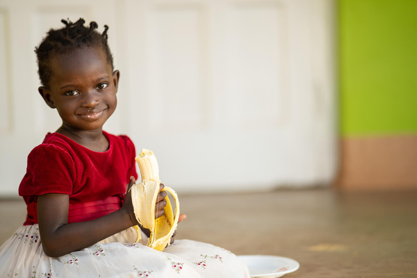 米や野菜など栄養価の高い昼食を取った後に、デザートのバナナを食べる3歳のエメラルドちゃん。(ウガンダ、2021年8月28日撮影)