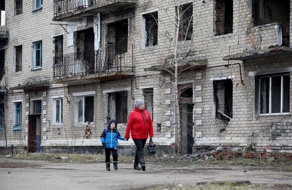 ドネツク州の小さな町で、戦闘により破壊された建物の前を歩く女性と子ども。(ウクライナ、2022年2月22日撮影／AFP)