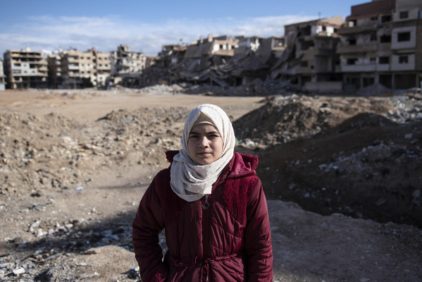 ダマスカスにて、紛争により破壊された街を背景に立つ11歳のアーミナさん。家族が働く建物が爆撃され父と兄を亡くした経験がトラウマとなり、突然の物音や動きが怖くなった。(シリア、2022年2月10日撮影)