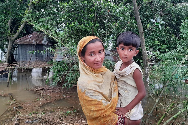 洪水で水浸しになり壊れてしまった家の前に立つ親子。母親のラクサナさんは「食料が手に入るかどうか不安です。ここにはトイレも飲み水もありません」と話す。(バングラデシュ、2022年5月16日撮影)
