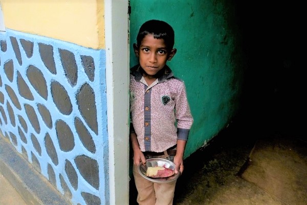ヌワラエリヤ(Nuwara Eliya)にある自宅で、お昼ご飯を手に持つ男の子。(スリランカ、2022年6月3日撮影)