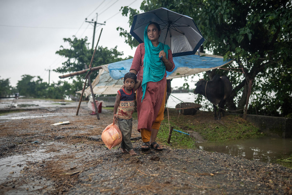 支援物資を受け取り、避難している近くの学校に戻る母親と5歳のセイモンちゃん。「9人家族なので、支援物資は足りない」と母親は話す。(バングラデシュ、2022年6月19日撮影)