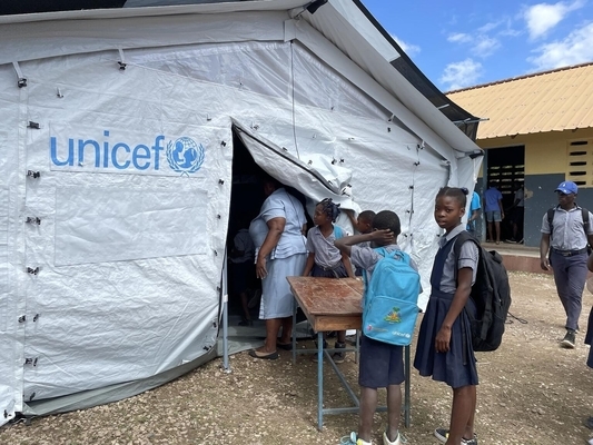 ユニセフの仮設テントの中に机を運ぶ子どもたち。(ハイチ、2022年2月撮影)