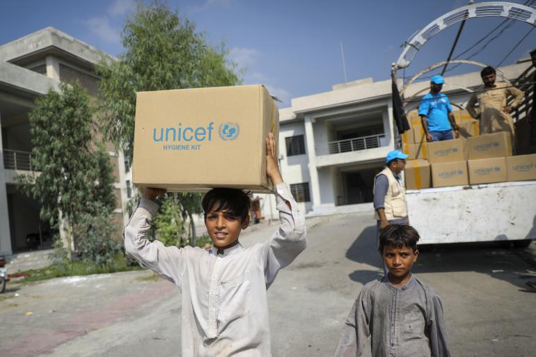 ユニセフの支援で配布されている衛生キットの箱を受け取ったアムジャドさん（14歳）。自宅が洪水に襲われた後、家族とともに一時的な避難キャンプで暮らしている。（パキスタンのハイバル・パフトゥンハー州、2022年8月30日撮影）