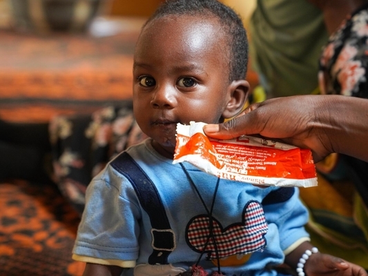 北ダルフールの国内避難民キャンプにある栄養ケア施設で、すぐに食べられる栄養治療食(RUTF)を口にする子ども。(スーダン、2022年8月2日撮影)