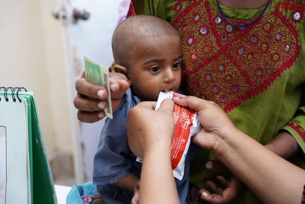 シンド州にある洪水の被害に遭った子どもたちのためのユニセフの栄養キャンプで、すぐに食べられる栄養治療食(RUTF)を口にする1歳のジャハンギルちゃん。(パキスタン、2022年9月14日撮影)