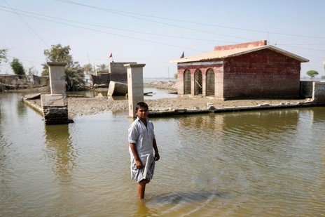 シンド州の浸水した学校の前に立つ8歳のシャヒドくん。一時は屋根まで浸水し、水位が下がってもまだ学校は再開できていない。(パキスタン、2022年10月30日撮影)