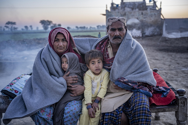 シンド州の自宅前で、ユニセフから受け取った毛布に包まり、身を寄せ合って暖を取る家族。(パキスタン、2023年1月4日撮影)
