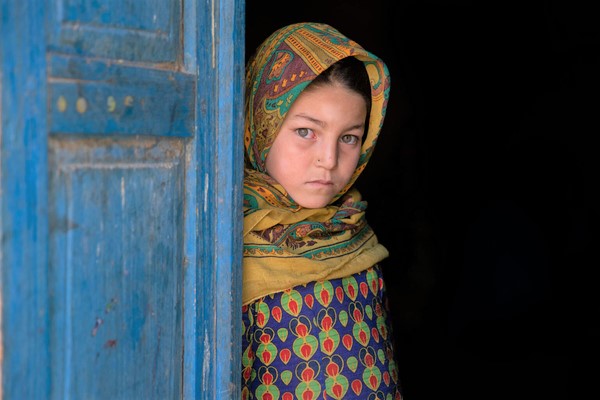 自宅のドアの前に立つ9歳のアスナさん。父親の稼ぎだけでは足りなく、現金給付支援を2回受け、米、小麦粉、油や必要な食料品を買うことができた。(アフガニスタン、2022年10月撮影)