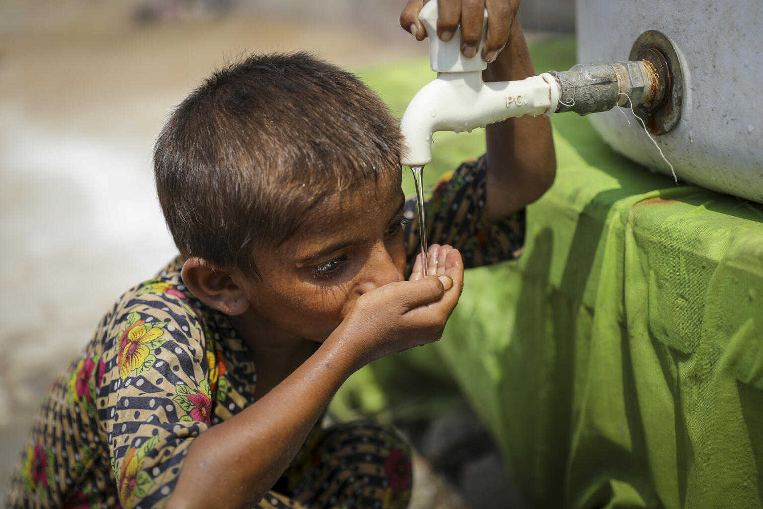 パキスタン全土を襲った未曾有の洪水で被災した子どもたちと家族のために、ユニセフが設置した給水タンクから水を飲む男の子（パキスタン、2022年9月11日撮影）