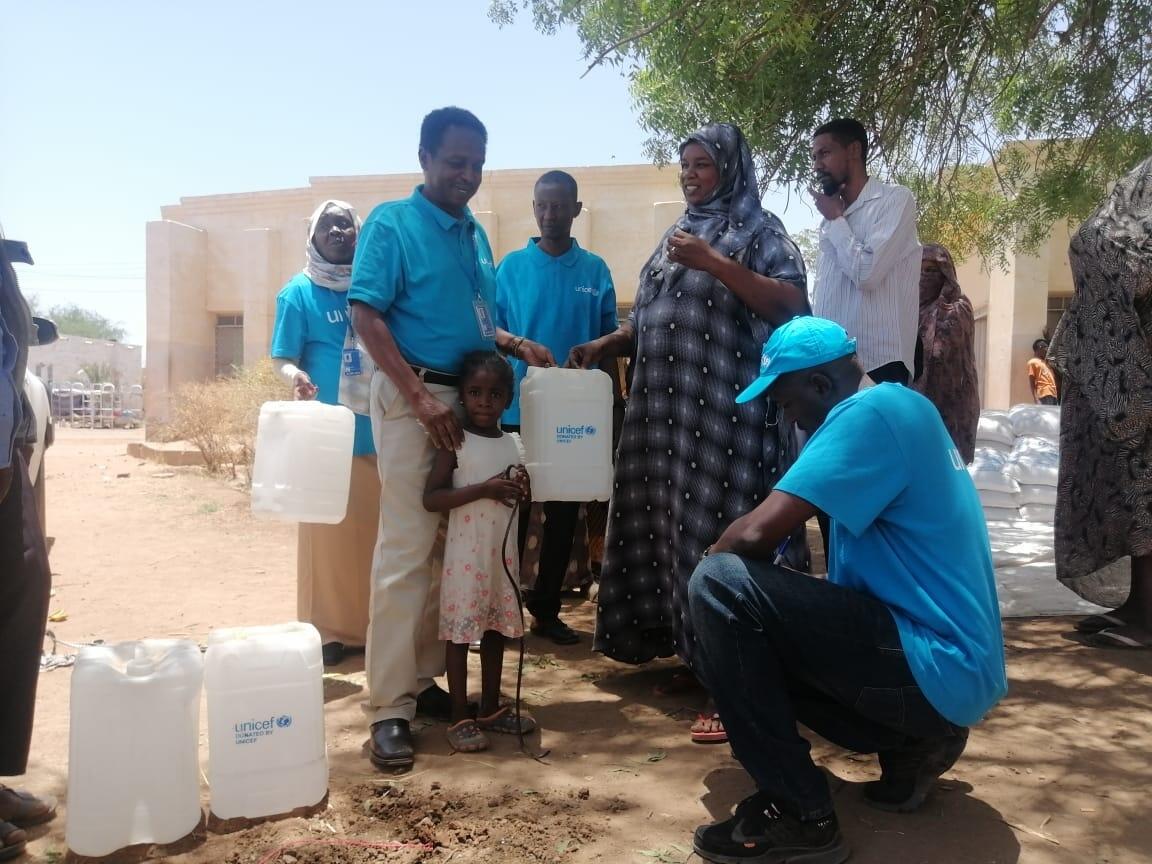 緊急対応の一環で、ハルツームからマダニに逃げて来た避難民の家族に水容器を配布するユニセフスタッフ（スーダン、2023年5月17日）