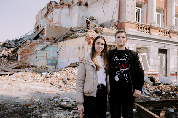 ハルキウ州で紛争の被害を受け、破壊された学校の前に立つ17歳のアナスタシアさんと12歳のミハイロさん姉弟。(ウクライナ、2023年4月撮影)