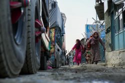 アフガニスタン・パキスタン国境にあるトールハムで、駐車中のトラックの前を走る女の子たち。