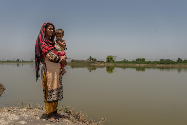 シンド州の村で、洪水により浸水した道の横にたつ親子。(パキスタン、2023年5月撮影)