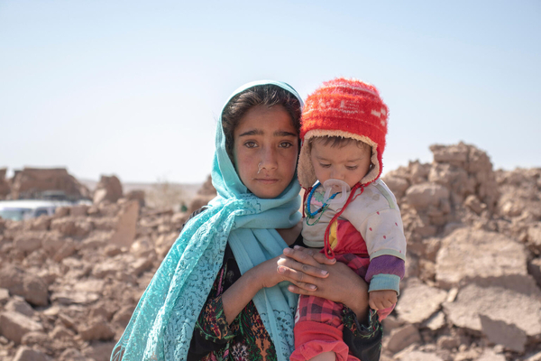 地震により倒壊した自宅の前で、生後8カ月の弟のマルブちゃんを抱く10歳のザリさん。(アフガニスタン、2023年10月10日撮影)