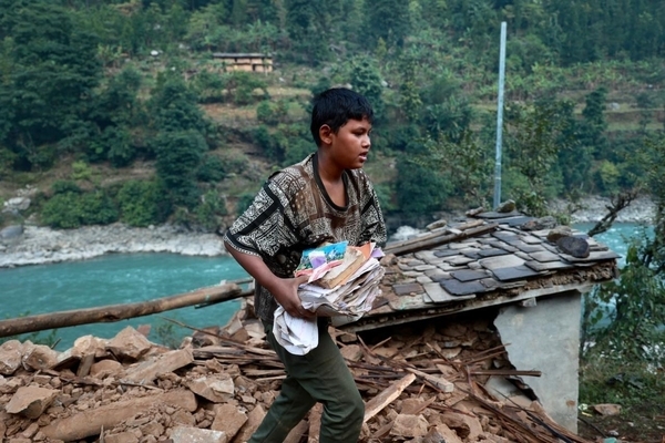 西ルクム郡で、地震により全壊した自宅から家財道具を運ぶ12歳のダーンラさん。「がれきになった家の中から本を数冊は取り出せた。学校にはいつ戻れるんだろう」と話す。(ネパール、2023年11月6日撮影)