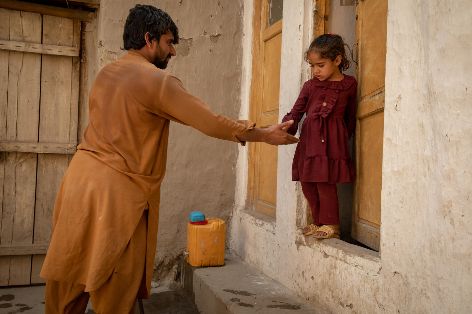 トイレを使った後のアスラちゃんに手を差し伸べるカマルディンさん（アフガニスタン、2023年6月19日撮影）