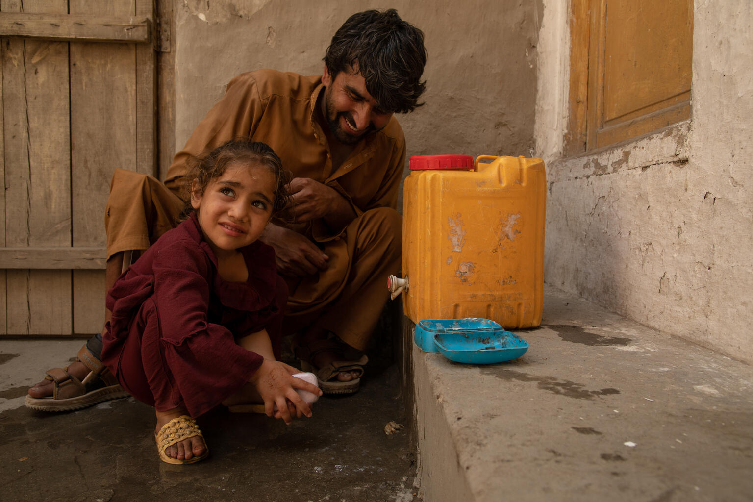 トイレの後、水の入った容器の前で、石けんを使って手を洗うアスラちゃん（アフガニスタン、2023年6月19日撮影）