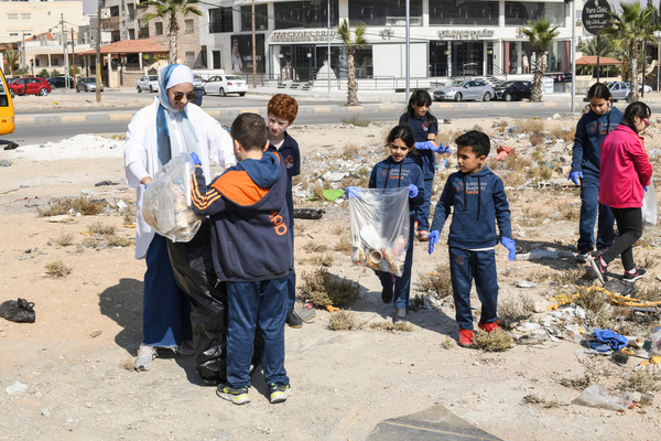 ザルカで、地域の清掃活動に参加する子どもたちと教員のエマンさん。ユニセフが支援するプログラムの若者の気候リーダーであるエマンさんは、生徒たちに環境保護の重要性を伝えている。(ヨルダン、2022年11月撮影)