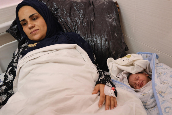 生まれたばかりの赤ちゃんとベッドで横になる母親。(ガザ地区、2024年1月12日撮影)
