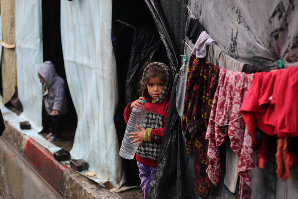 ラファの避難所のテント前で、空のペットボトルを手に持つ女の子。(ガザ地区、2024年1月31日撮影)