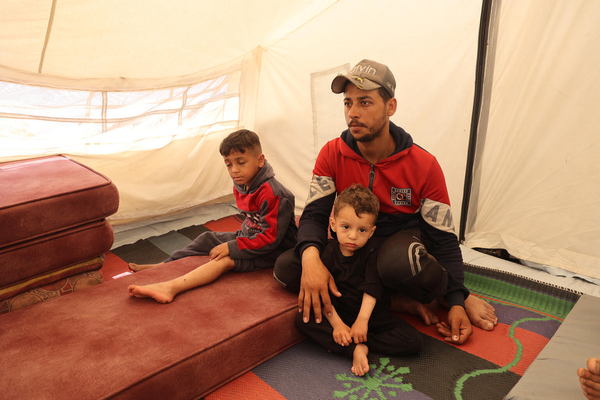 ラファにある避難所のテントの中で、父親と過ごす7歳のアミールさん(左)と2歳の従弟。母親はガザ北部にいるため離れ離れになっている。アミールさんは学校に避難したときに右脚を負傷し、あと数回の手術が必要な状態である。(ガザ地区、2024年4月14日撮影)