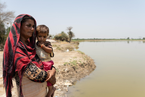 シンド州の村で、浸水した道の横に立ち3歳のオマーラちゃんを抱く母親。洪水により子どもをひとり亡くした。生活も困窮しており、1日1回わずかな食事しかとれていない。(パキスタン、2023年5月撮影)