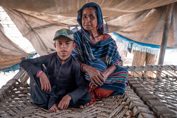 洪水により家が破壊され、木と防水シートで作ったその場しのぎのテントで生活する8歳のモハンマドさんと母親。汚染された水による腸の感染症が原因で、兄弟がひとり亡くなった。(パキスタン、2024年7月撮影)