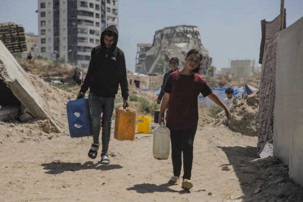 ガザの海岸沿いにある一時避難所で寝起きをしている10歳のハラさん（右）。支援の給水車を待ち、家族が使うための水を運ぶのが毎朝の日課。しかし、多くの人が避難しており、運ばれてくる水の量が十分でないこともよくある（パレスチナ、2025年5月23日撮影）