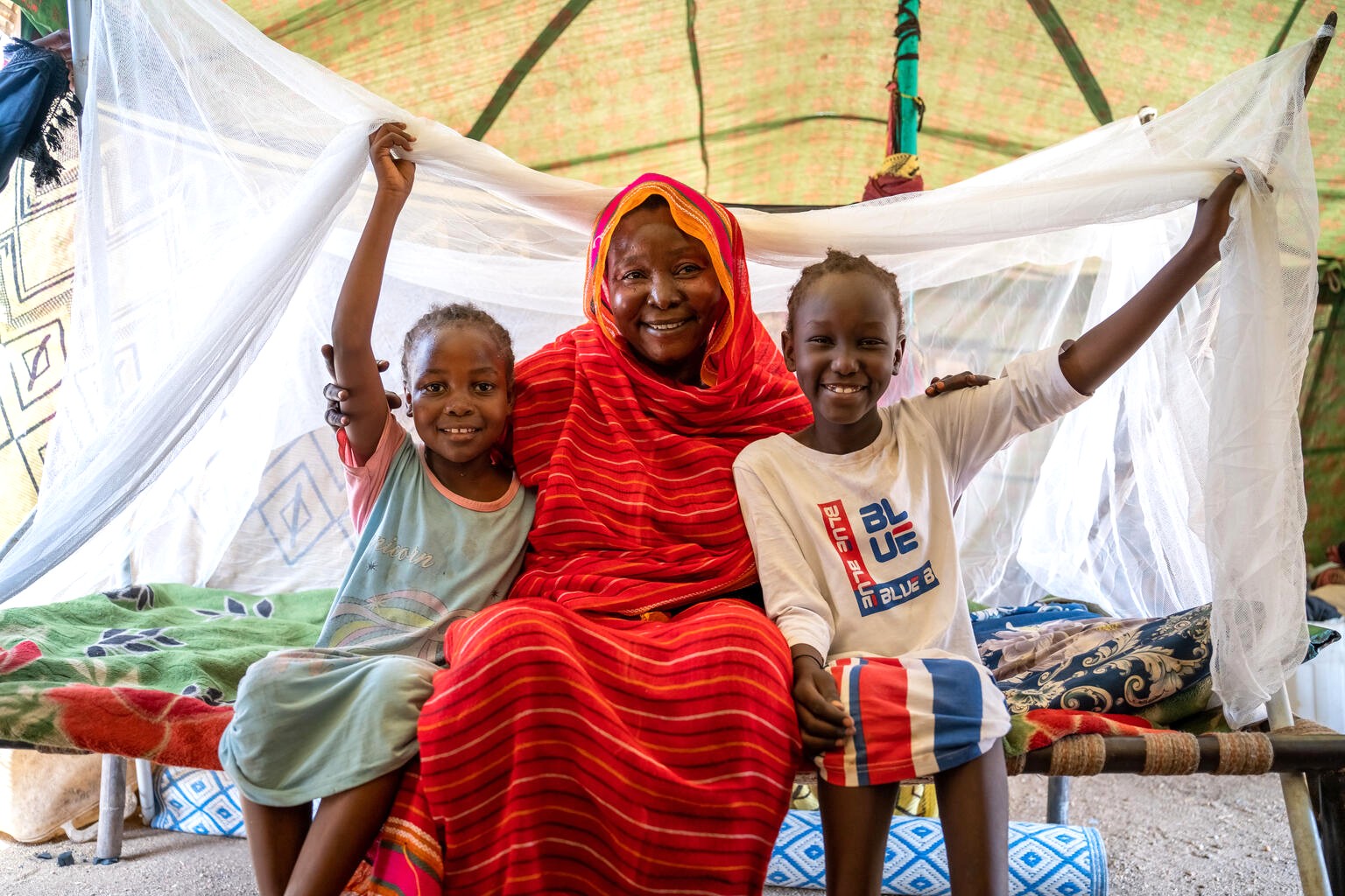 新しい蚊帳を寝床に設置したバディアさんと子どもたち（スーダン、2025年5月30日撮影）