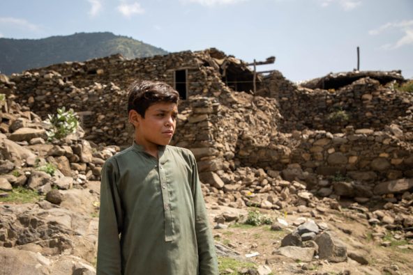 地震により倒壊した、クナール県の自宅前に立つ男の子（アフガニスタン、2025年9月2日撮影）