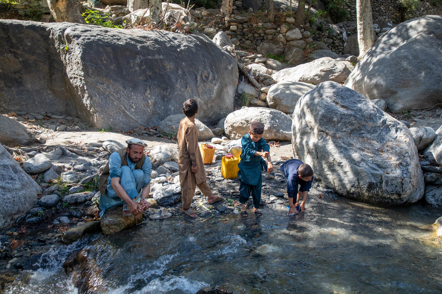 クナール県で、仮設シェルターで寝起きをしている家族が、小川で水をくむ様子（アフガニスタン、2025年10月14日撮影）