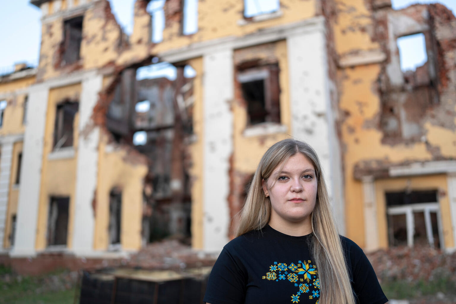 ハルキウで、がれきと化した学校の前に立つ17歳のソフィアさん。将来の夢は、子どもたちの命を救う医師になること（ウクライナ、2025年8月16日撮影）