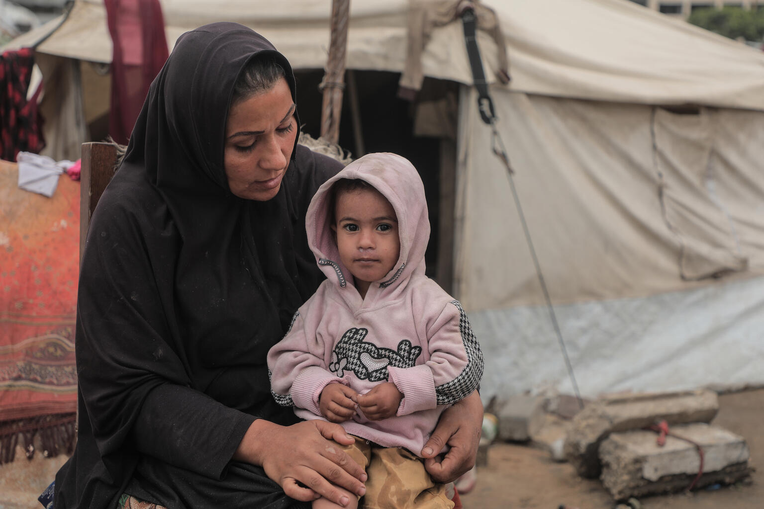 寝起きしているテントの中に雨水が浸水し、寒さに凍える娘を抱くマイサーさん。「これからの冬の季節をどうやって生きのびたらいいのか」と嘆く（パレスチナ、2025年11月14日撮影）