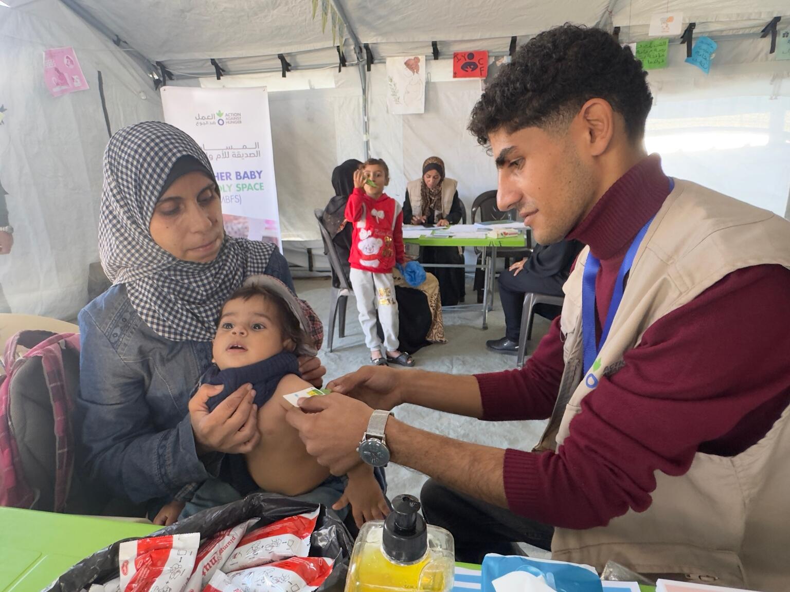 ユニセフが支援する栄養治療拠点で、上腕計測メジャーを使った検査を受ける1歳のモアタズちゃん。急性栄養不良と診断されていたが、8週間の治療を経て回復しつつある(パレスチナ、2025年12月2日撮影)