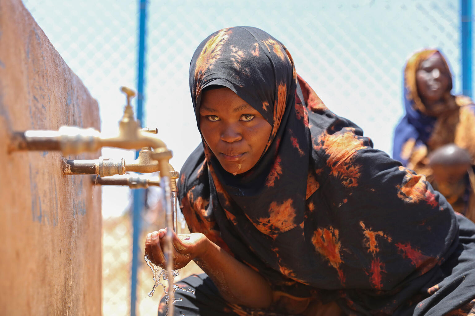 南部ドローにある国内避難民キャンプの給水所で水を飲む女性。深刻な干ばつで住み慣れた場所を離れざるをえなかった人々も、キャンプに避難してきている(ソマリア、2026年3月25日撮影)