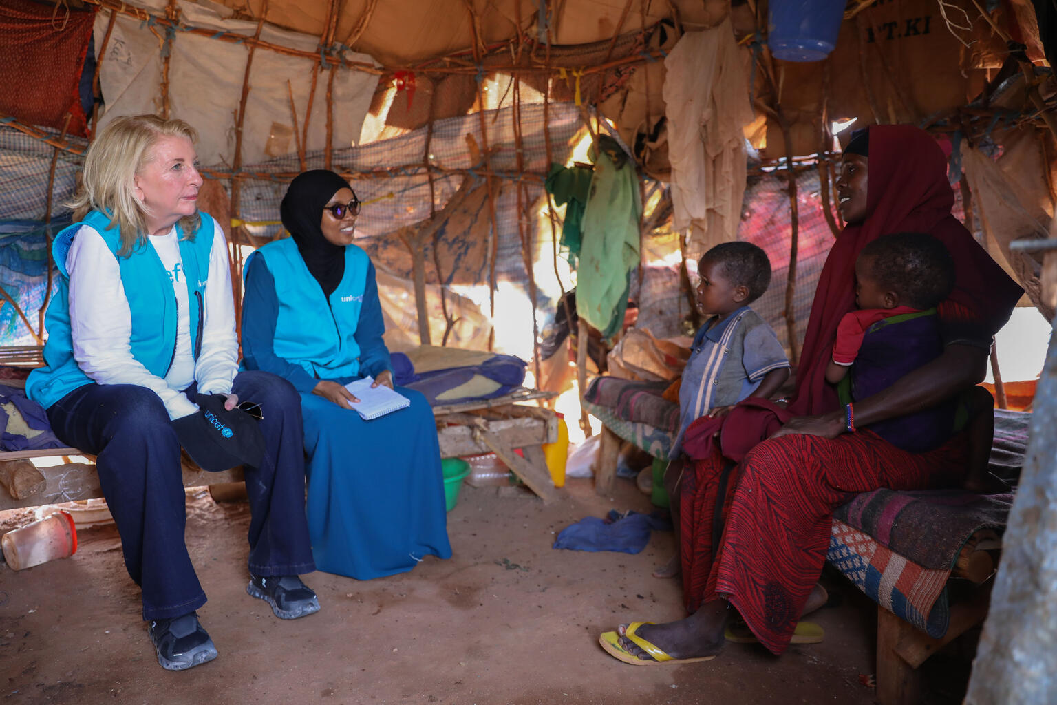 南部ドローの国内避難民キャンプで、自身の経験を語るハビバさん(右端)の話に耳を傾けるラッセル事務局長(左端)。ハビバさんは干ばつの影響で家畜と農作物を失い、栄養不良に陥った子どもたちを助けてもらうため、7日間も歩き続けてドローにたどり着いた(ソマリア、2026年3月25日撮影)